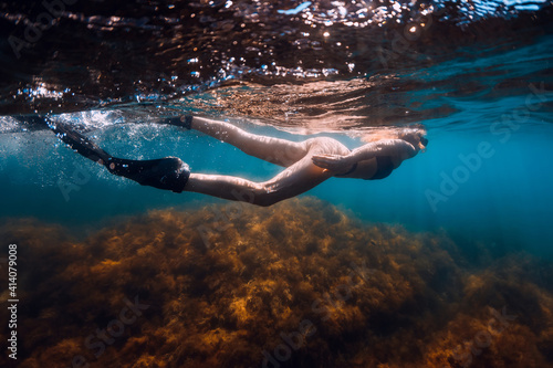 Young woman with fins and mask swim in blue sea with sun rays. Snorkeling underwater in summer ocean