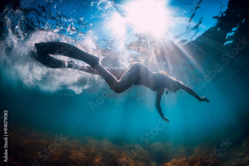 Young woman with fins and mask swim in blue sea with sun rays. Snorkeling underwater in summer ocean