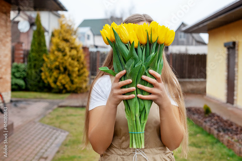 The girl hides her face behind a large bouquet of yellow tulips. Women's Day, Valentine's Day, Mother's Day.
