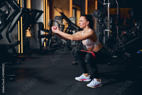 Happy young woman doing squats in gym
