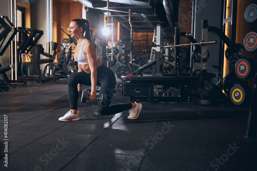Joyful young woman doing lunges with weights