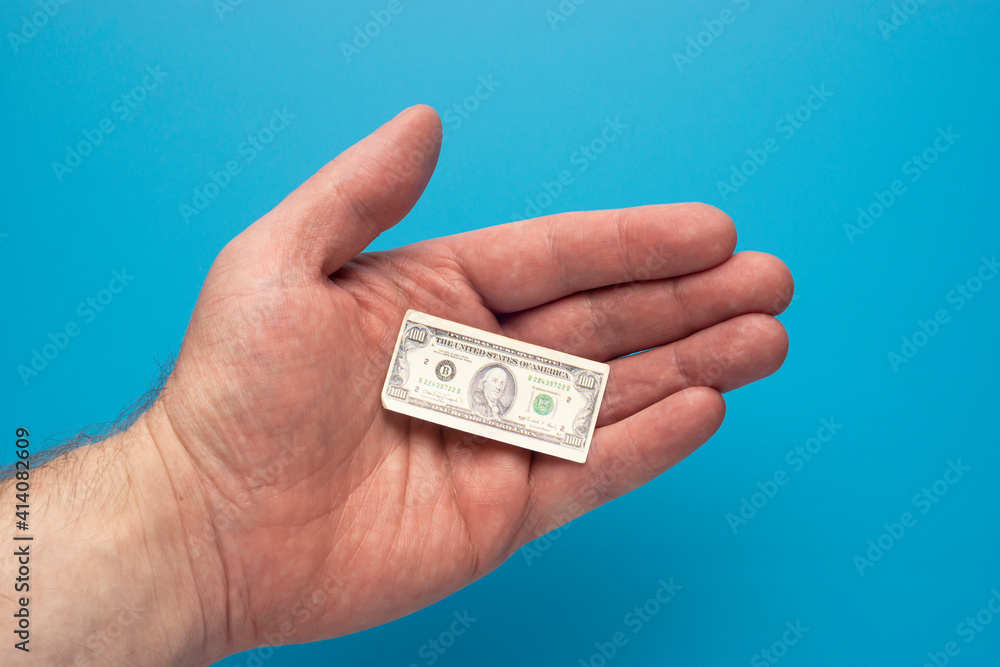 Toy tiny hundred dollar bill in open palm of a man, financial concept Toy tiny hundred dollar bill in open palm of a man, financial concept