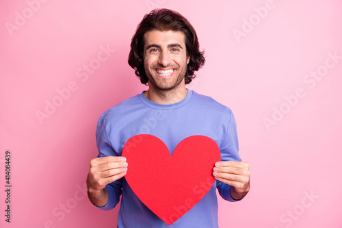 Portrait of charming man hands hold large heart shape purple pullover isolated on pink color background © deagreez