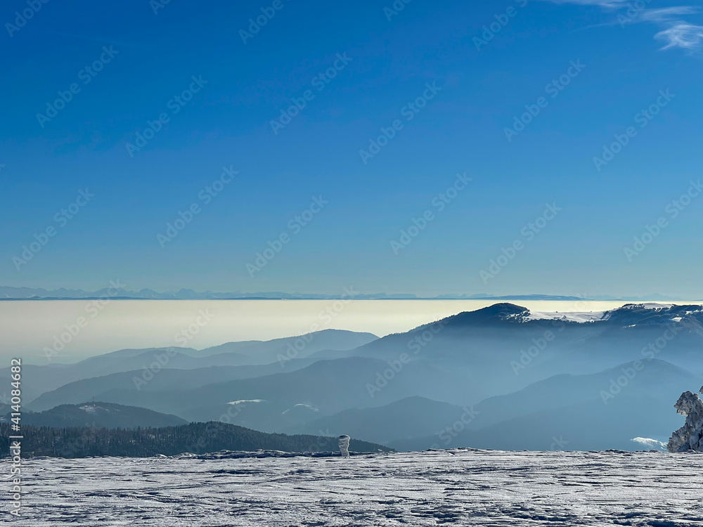 View of a distant mountain range (the Alps) from other snow-capped mountains (the Vosges) with a sea of clouds