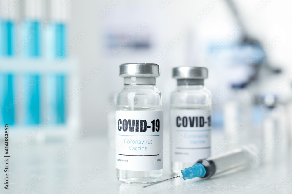 Vials with vaccine against Covid-19 and syringe on white table indoors Vials with vaccine against Covid-19 and syringe on white table indoors