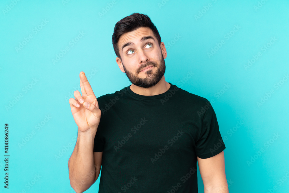 Caucasian handsome man isolated on blue background with fingers crossing and wishing the best Caucasian handsome man isolated on blue background with fingers crossing and wishing the best