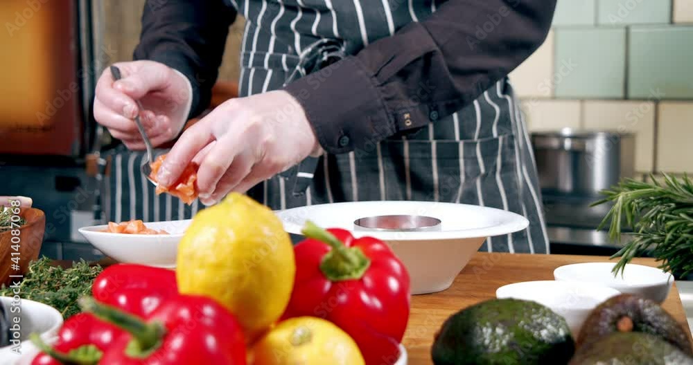 Close-up of male chef hands in gloves preparing delicious tartare from fresh vegetables and salmon fillets in the kitchen. Healthy and organic food. Shooting through the foreground. Close-up of male chef hands in gloves preparing delicious tartare from fresh vegetables and salmon fillets in the kitchen. Healthy and organic food. Shooting through the foreground.
