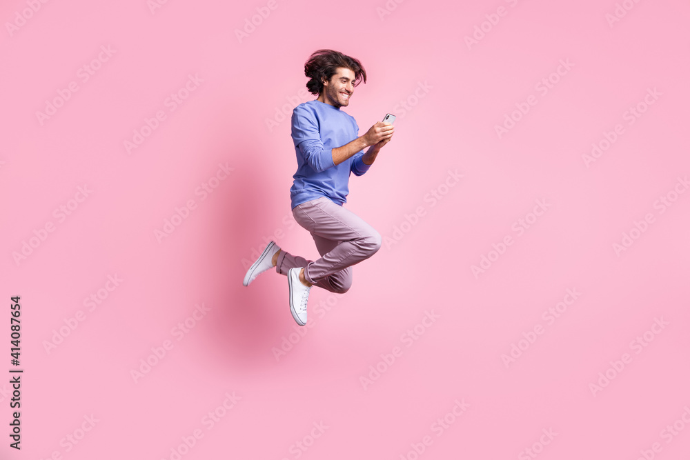 Full size photo of young happy smiling handsome positive man jump fly use smartphone isolated on pink color background Full size photo of young happy smiling handsome positive man jump fly use smartphone isolated on pink color background