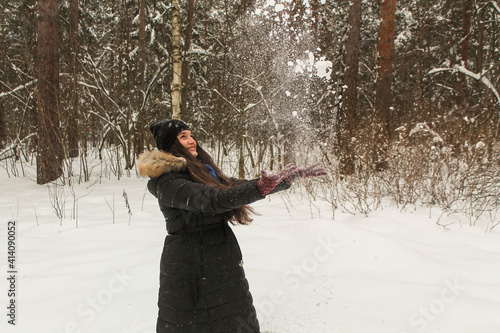 Girl with long hair in the forest in winter throws snow