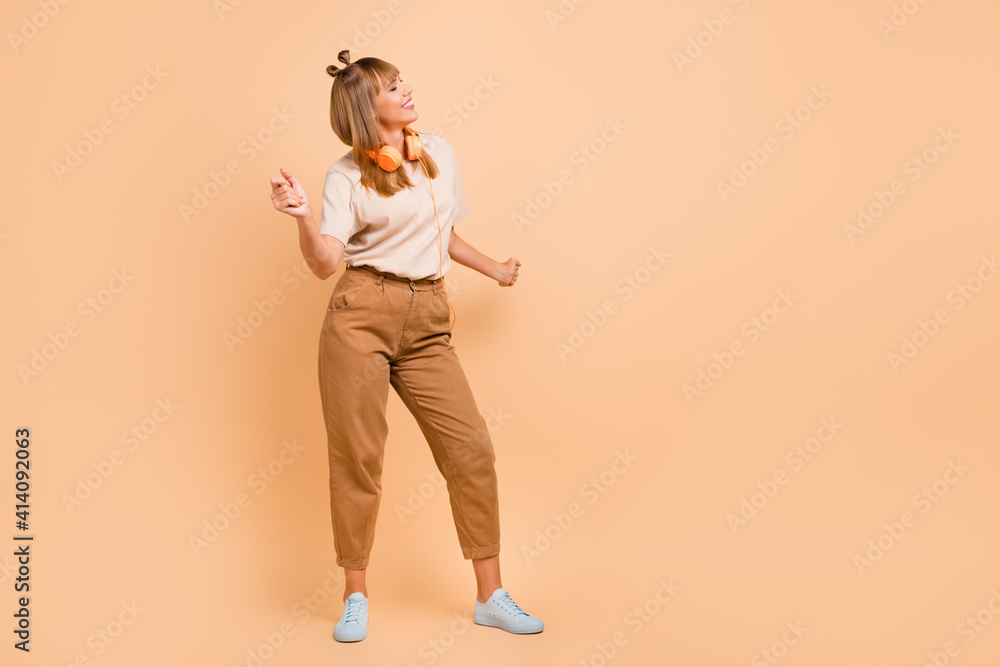 Fototapeta premium Full length photo of cute girl enjoy dancing close eyes wear earphones t-shirt isolated beige color background