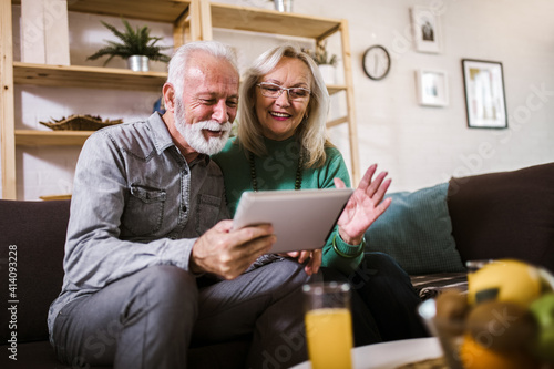 Happy senior couple having video chat with tablet computer in living room