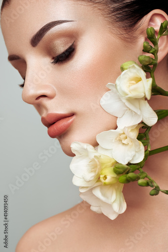 Beautiful model with a flower. Perfect woman face makeup close up. Lipstick. Eyelashes. Glowing skin