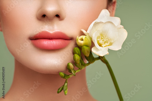 Beautiful model with a flower. Perfect woman face makeup close up. Lipstick. Eyelashes. Nice smile. Glowing skin