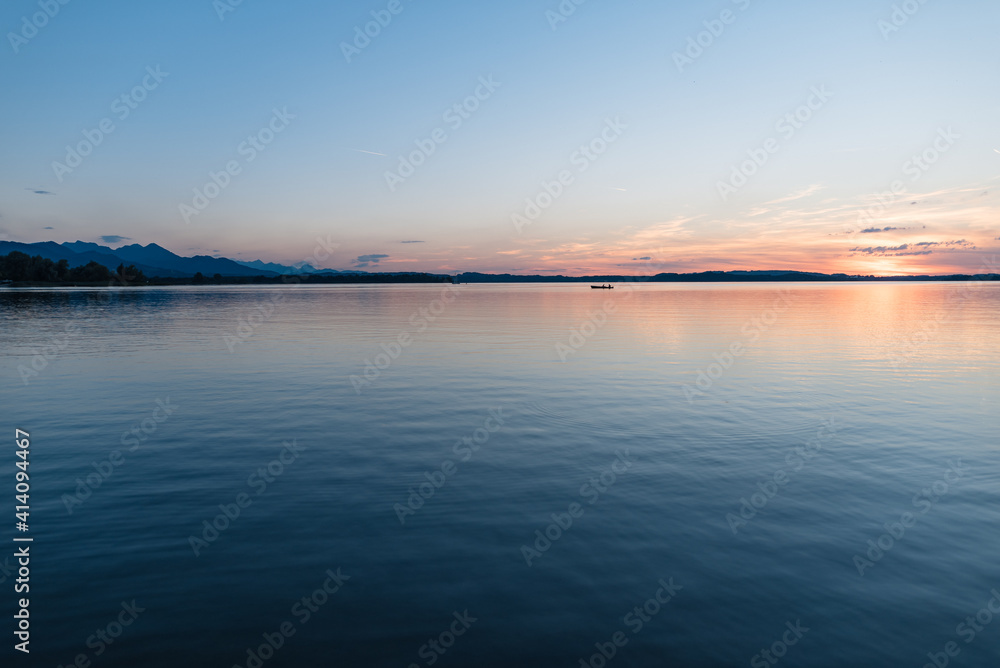 Abendstimmung im Sommer am Chiemsee in Bayern - blauer Himmel mit Sonnenschein am Horizont über ruhigem Wasser