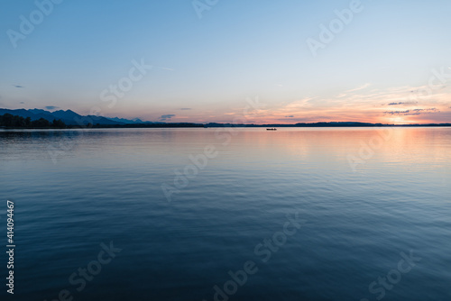 Abendstimmung im Sommer am Chiemsee in Bayern - blauer Himmel mit Sonnenschein am Horizont über ruhigem Wasser