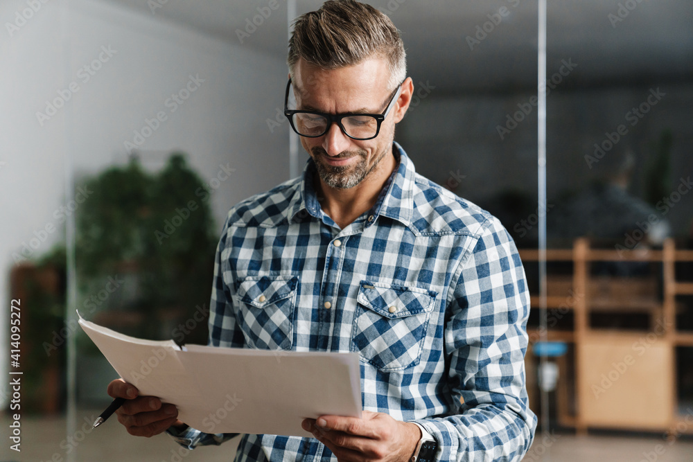 Joyful white-haired man working with papers while standing in office Joyful white-haired man working with papers while standing in office