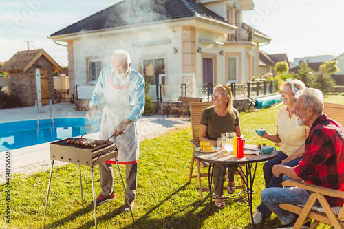 Elderly neighbors having backyard barbecue party by the swimming pool