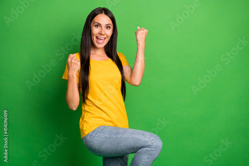 Photo of astonished young woman raise fists celebrate lucky win isolated on funky green color background