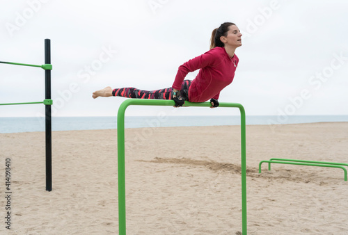 Fitness woman doing hand stand exercises on callisthenics outdoor gym bars.Beach workout, sports training lifestyle concept.