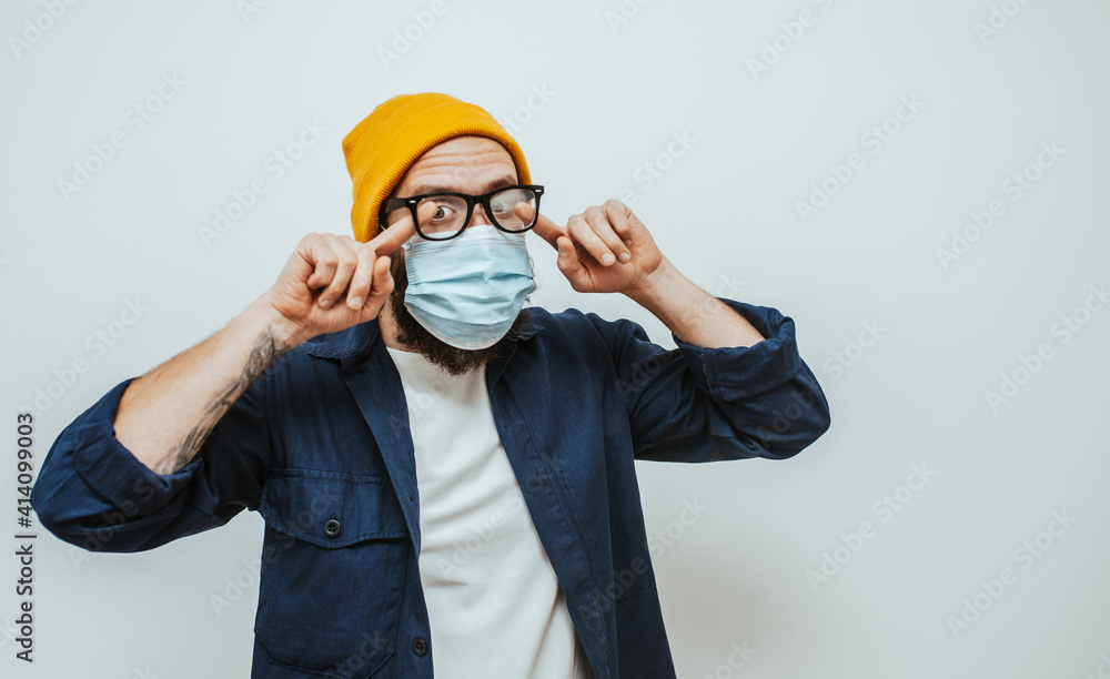 Handsome man with beard wiping blurred foggy misted glasses caused by wearing medical mask on light background. Covid-19 Handsome man with beard wiping blurred foggy misted glasses caused by wearing medical mask on light background. Covid-19