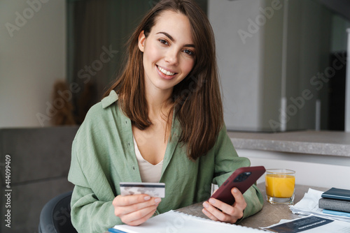 Happy woman using mobile phone and credit card while working with papers