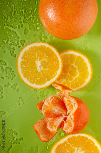 Vertical image of fresh and juicy fruits on the wet green surface.Natural and ripe oranges  tangerine  whole grapefruit