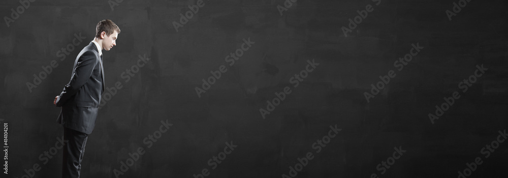 Young businessman looking at an empty space for text over black wall