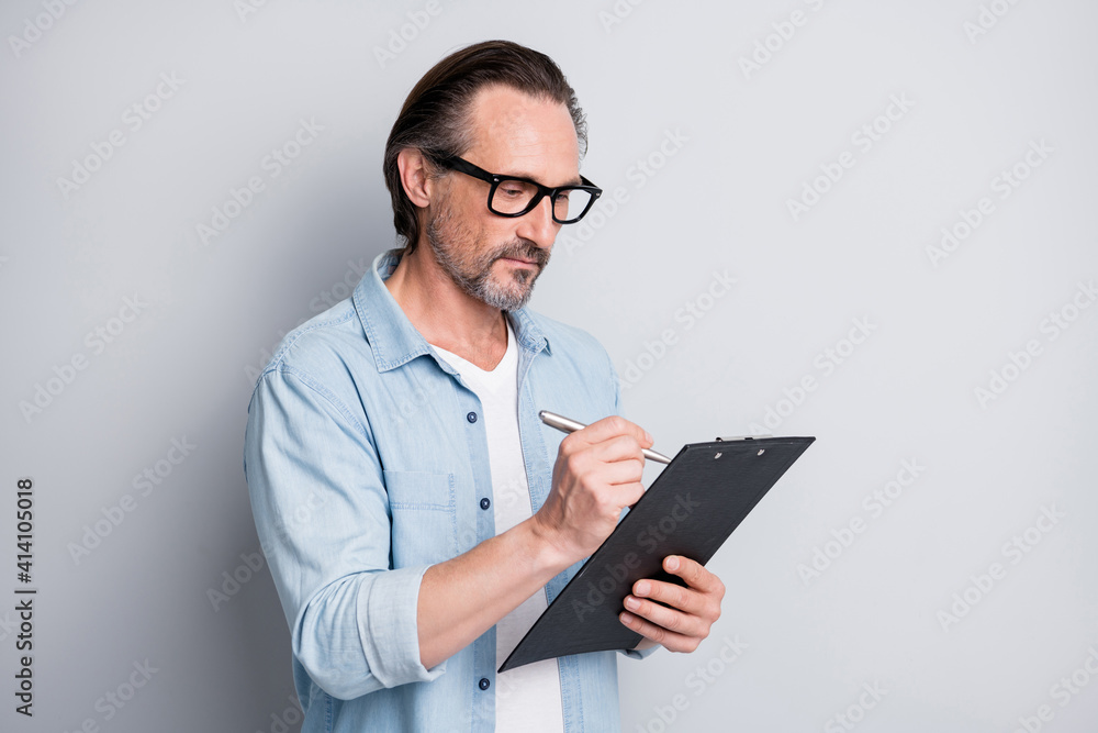 Photo of handsome man hold clipboard writing wear glasses serious face isolated on grey color background Photo of handsome man hold clipboard writing wear glasses serious face isolated on grey color background