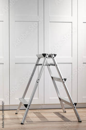 The folding ladder for repair and installation of furniture stands on a wood floor. Repair