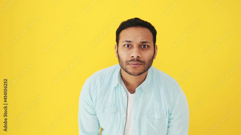 An attractive indian man is peeping for something standing isolated over yellow background in studio An attractive indian man is peeping for something standing isolated over yellow background in studio