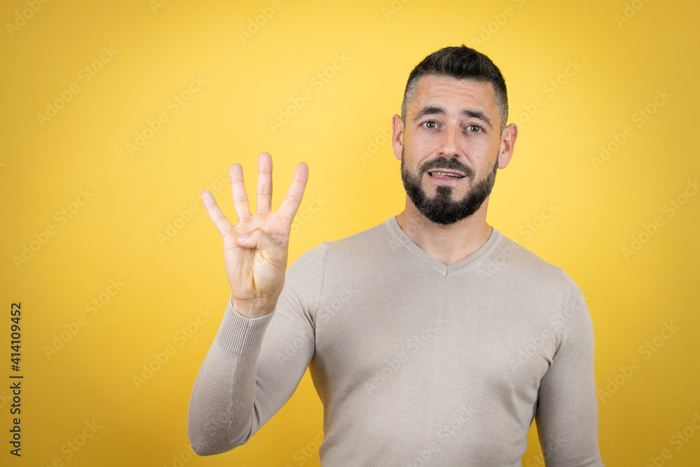 Handsome man with beard wearing sweater over yellow background showing and pointing up with fingers number four while smiling confident and happy Handsome man with beard wearing sweater over yellow background showing and pointing up with fingers number four while smiling confident and happy