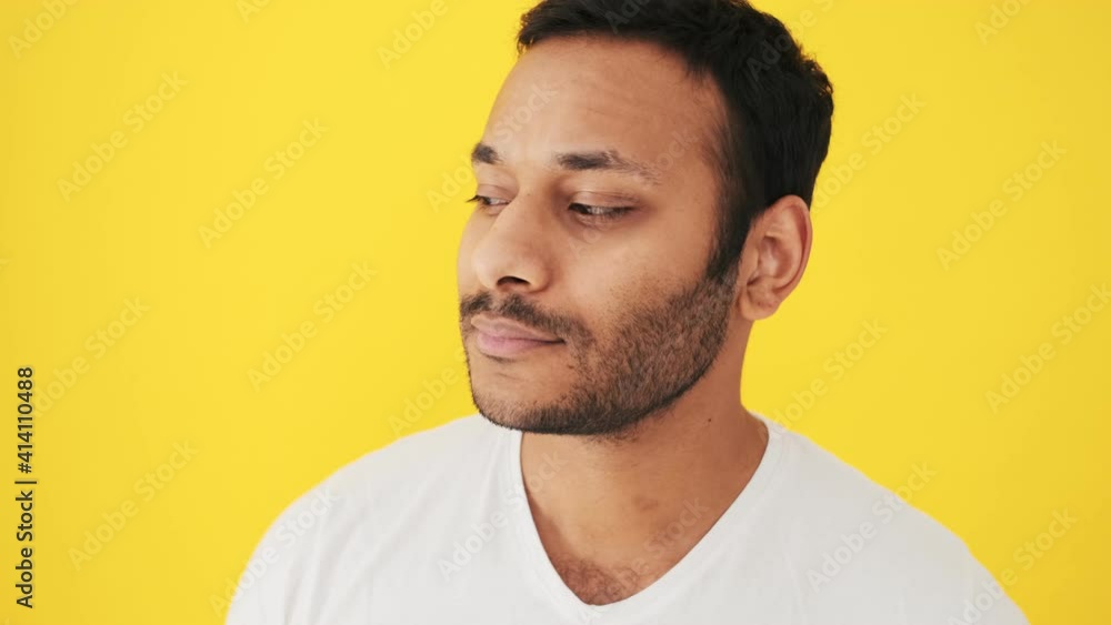 A close-up view of a calm indian man is looking to the camera standing isolated over yellow background in the studio A close-up view of a calm indian man is looking to the camera standing isolated over yellow background in the studio