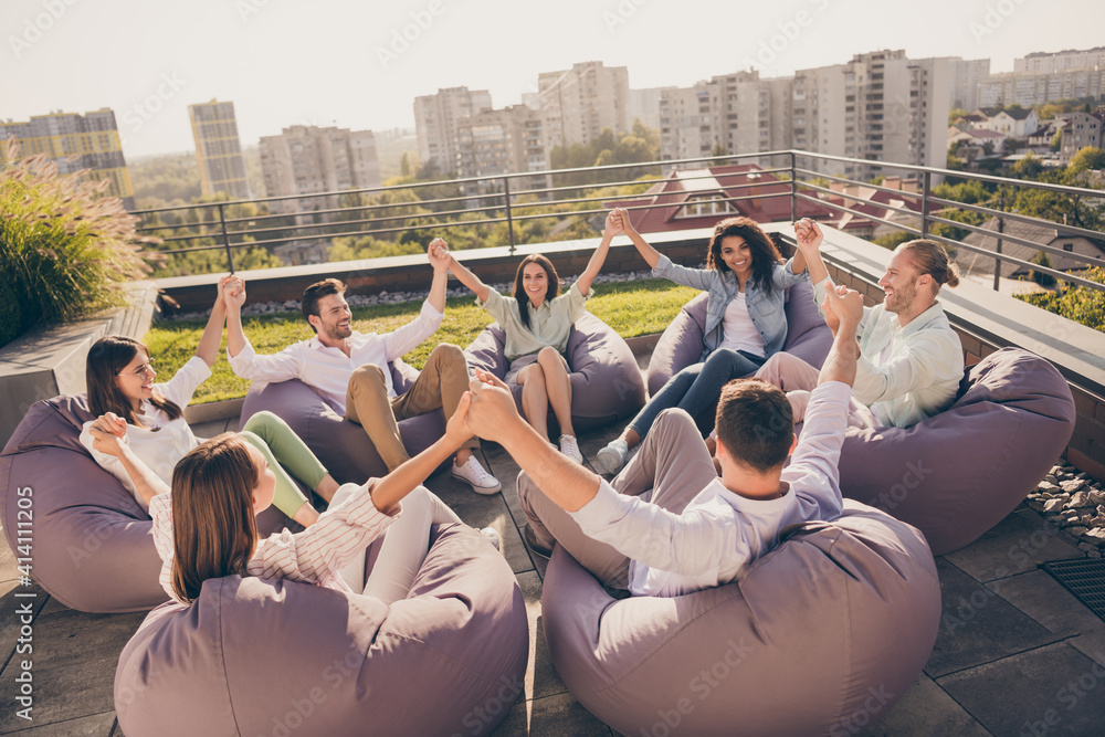 Photo of happy agents sitting beanbags corporate trust training rising arms workplace workstation outdoors outside urban terrace