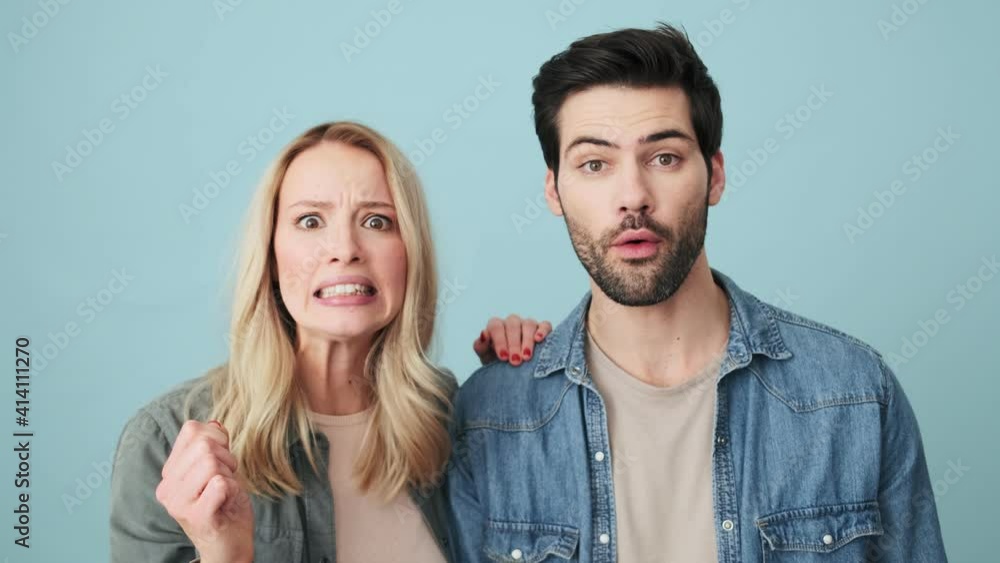 Happy couple man and woman are doing winner gesture standing isolated over blue background in studio Happy couple man and woman are doing winner gesture standing isolated over blue background in studio