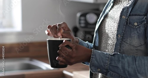 Young woman standing in kitchen, stirring hot drink, close-up photo