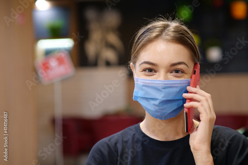 Young girl in blue medical protective mask talks on smartphone inside restaurant photo