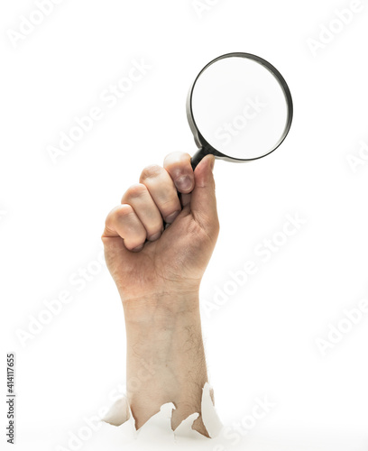 Concept of finding. Man's hand with magnifying glass stick out of hole in paper. Isolated on white.