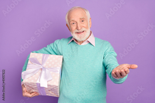 Photo portrait of senior man keeping present box with present smiling inviting to party isolated on pastel purple color background
