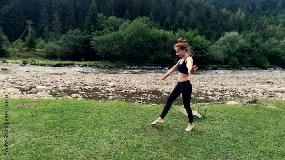 Girl athlete performing acrobatic cartwheel on grass near river