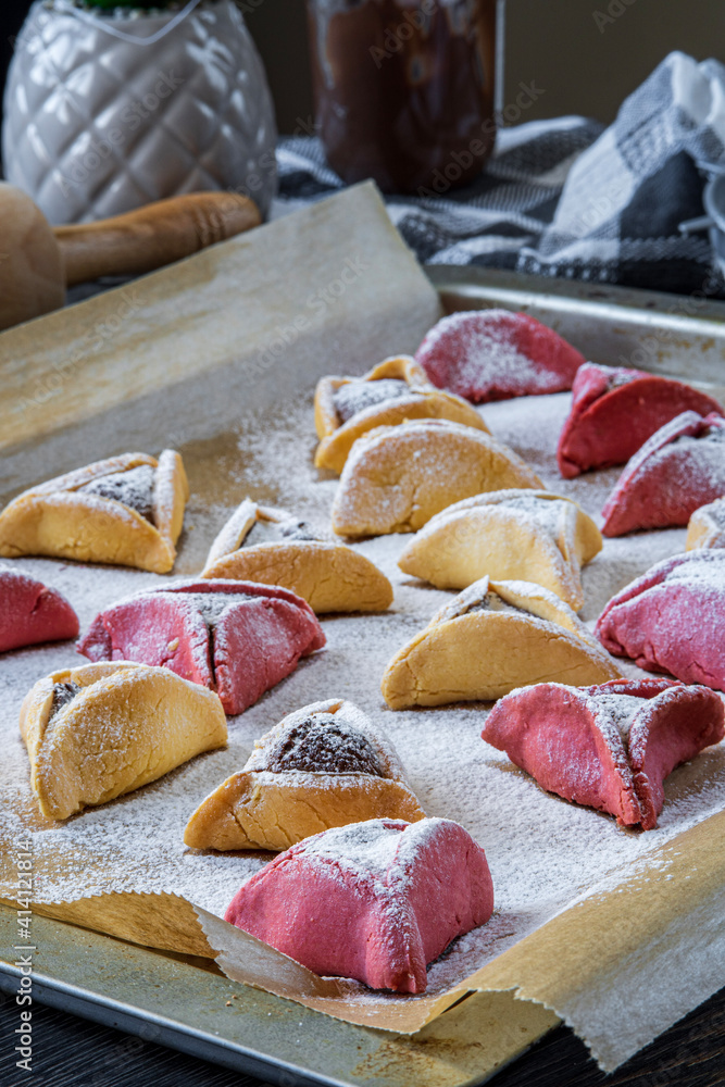 Colorful hamantaschen cookies on a baking tray in the kitchen. Jewish traditional pastry for Purim (Jewish carnival holiday with celebration concept). Homemade gluten free cookie filled with chocolate Colorful hamantaschen cookies on a baking tray in the kitchen. Jewish traditional pastry for Purim (Jewish carnival holiday with celebration concept). Homemade gluten free cookie filled with chocolate