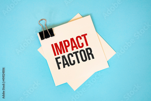 Text IMPACT FACTOR on sticky notes with copy space and paper clip isolated on red background.Finance and economics concept.