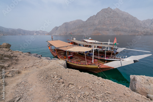 Two traditional arab dhow boats parked by an island in turquoise fjords of Musandam, Oman. Hot, hazy day in fjords of Arabia.