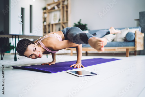 Strong female in casual sportive wear standing in asana on carpet stretching body keeping muscular strength  fit girl enjoying morning yoga for training flexibility in modern home interior