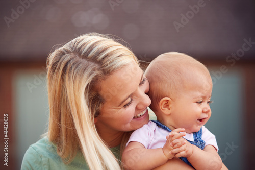 Loving Mother Cuddling Smiling Baby Daughter Outside House