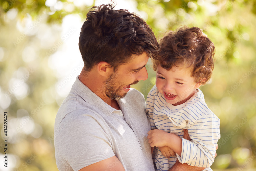 Loving Father With Son Having Fun In Park Holding Him In The Air Against Leafy Background Loving Father With Son Having Fun In Park Holding Him In The Air Against Leafy Background