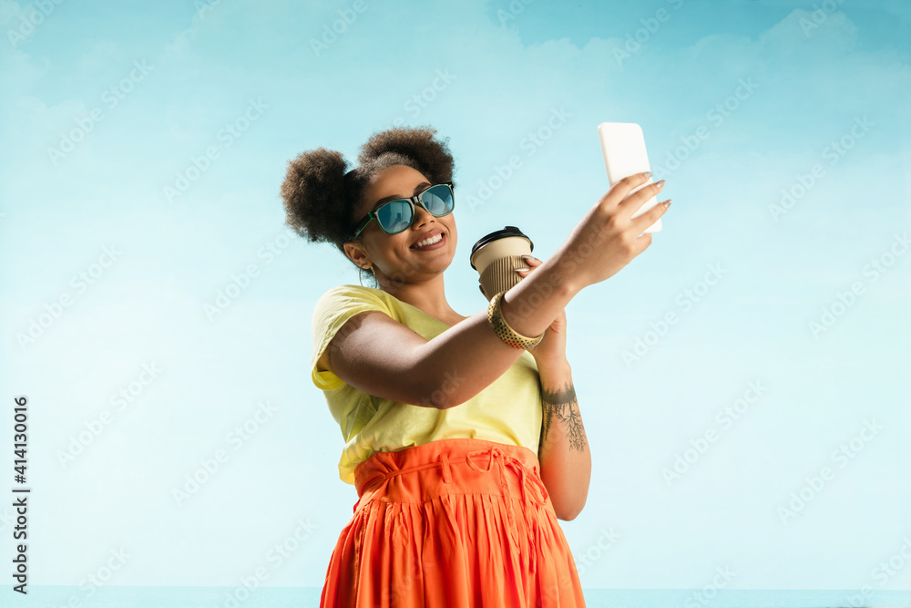 © master1305 - Selfie. Portrait of young female fashion model on blue sky background. Beautiful african woman with trendy make-up and bright appearance. Style and beauty concept, summer mood. Copyspace for ad. © master1305 - Selfie. Portrait of young female fashion model on blue sky background. Beautiful african woman with trendy make-up and bright appearance. Style and beauty concept, summer mood. Copyspace for ad.