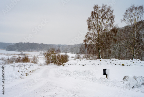 An icy and snowy winter road going through a meadow and forest landscape. Picture from Scania, southern Sweden