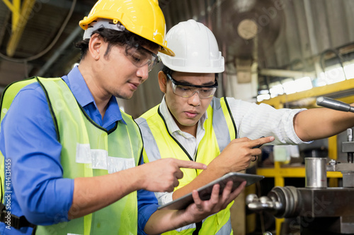 Engineers and skilled technicians are maintaining machinery. Professional technicians are holding a tablet to control work in industrial plants
