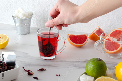 Woman stiring sugar in the tea cup.Fresh lemon, lime and grapefruit, herbal tea leaves on the white table photo