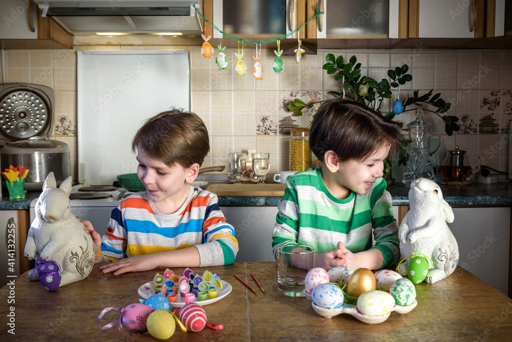 Fototapeta premium Two little kid boy coloring eggs for Easter holiday in domestic kitchen, indoors. Sibling brothers having fun and celebrating feast